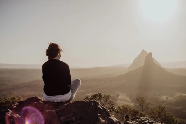 Person sitting peacefully on a large rock in nature