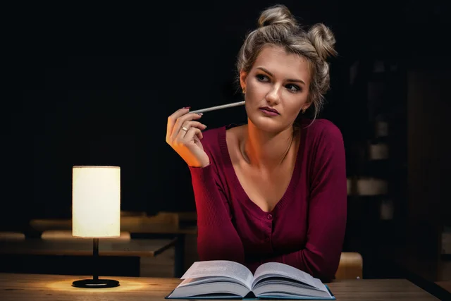 Woman studying at a desk with books and a lamp